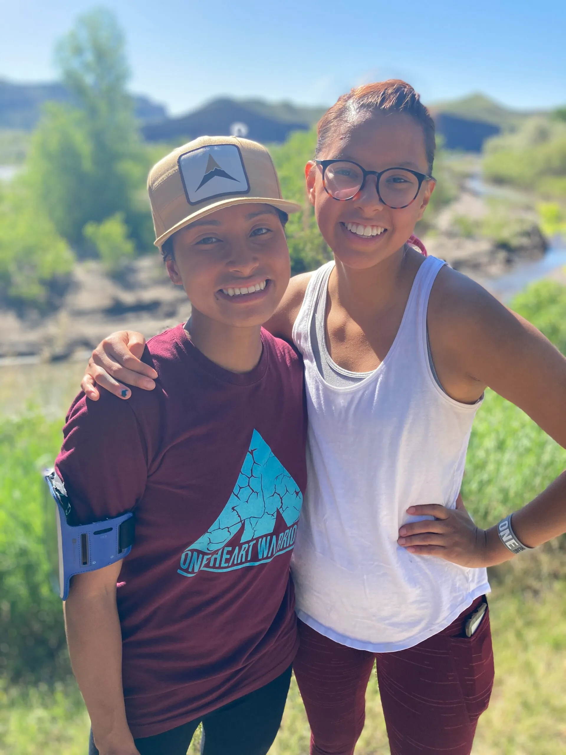 Two smiling young women wearing One Heart Warriors branded apparel, representing youth development and leadership in Native communities.